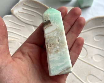 May include: A green and white agate crystal point with brown inclusions. The crystal is polished and has a smooth, glassy surface.