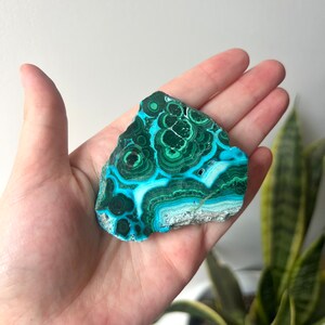 May include: A green and blue azurite malachite crystal with a swirling pattern. The crystal is a natural stone and has a rough, irregular shape.