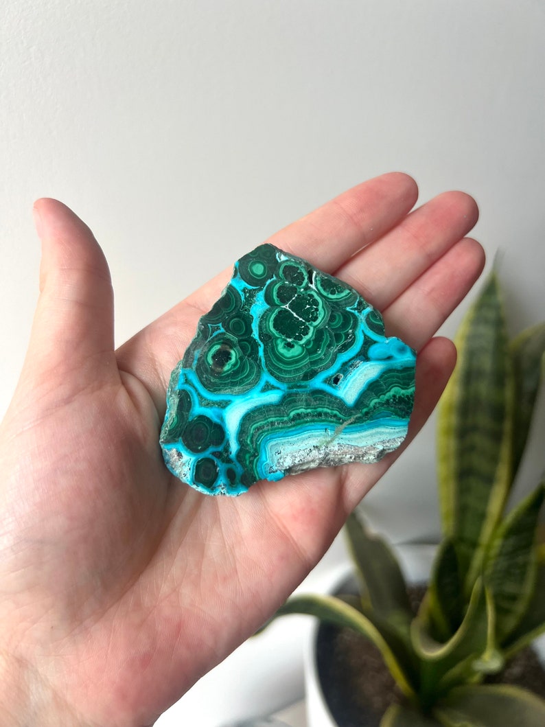 May include: A green and blue azurite malachite crystal with a swirling pattern. The crystal is a natural stone and has a rough, irregular shape.