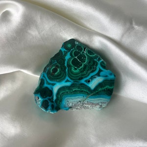 May include: A green and blue malachite stone with a swirling pattern. The stone is smooth and polished.