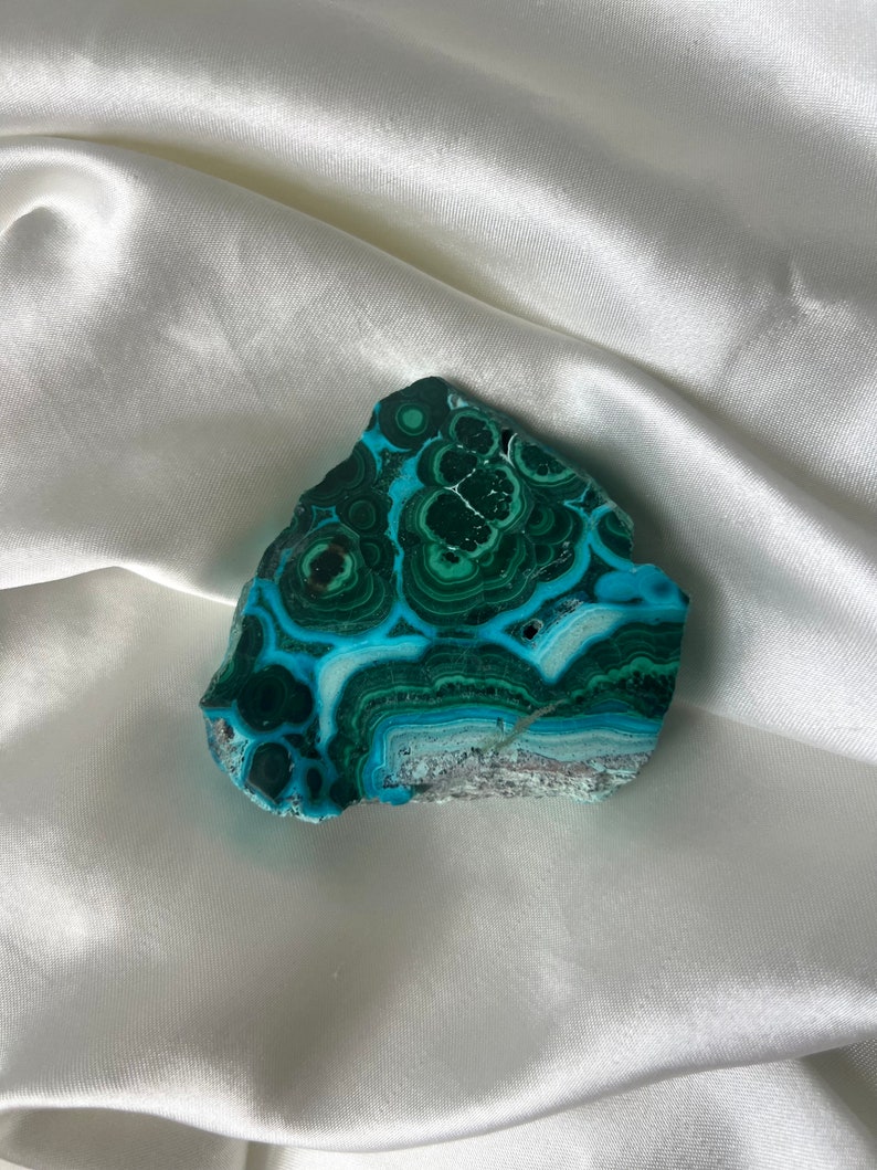 May include: A green and blue malachite stone with a swirling pattern. The stone is smooth and polished.
