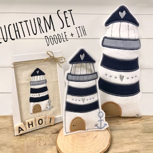 May include: A set of two white and blue lighthouse-themed embroidery designs. The larger design is a plush pillow with a blue and white striped lighthouse, a small anchor, and a heart on top. The smaller design is a framed embroidery with a similar lighthouse design. The text "LEUCHTTURM SET DOODLE + ITH" is at the top of the image. The text "AHOI" is spelled out with wooden blocks at the bottom of the image.