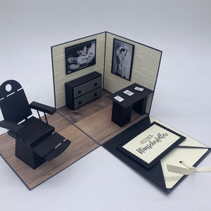 May include: A black and white pop-up card with a tattoo parlor theme. The card features a black leather chair, a small desk with a lamp, and a framed photo of a tattoo artist working on a client. The card is open and the inside reads "Kleiner Wunschzettel f&uuml;r".