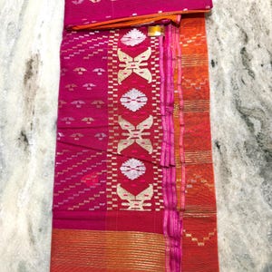May include: A vibrant pink textile with intricate patterns and gold accents. The fabric features geometric designs, including diagonal lines and stylized floral motifs. The border is a contrasting orange hue, adding visual interest to the overall design.