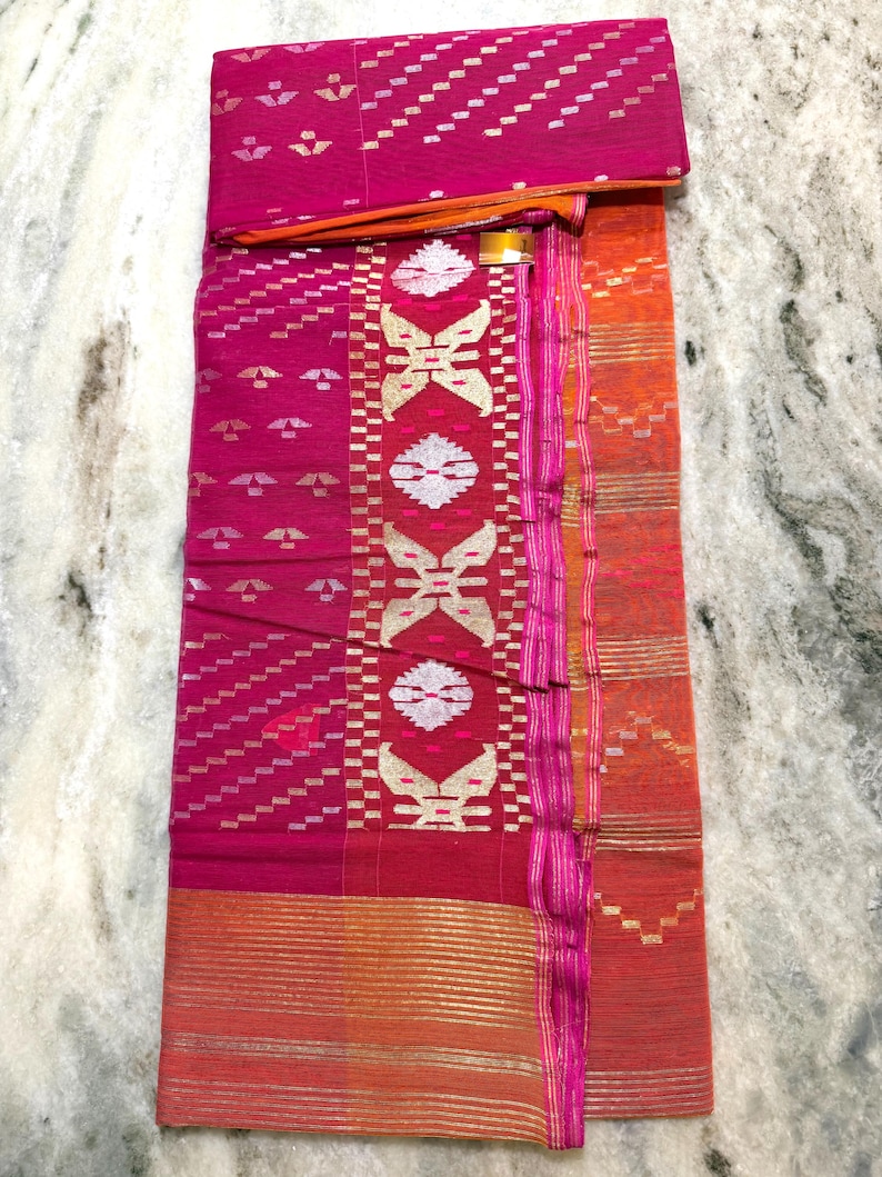 May include: A vibrant pink textile with intricate patterns and gold accents. The fabric features geometric designs, including diagonal lines and stylized floral motifs. The border is a contrasting orange hue, adding visual interest to the overall design.