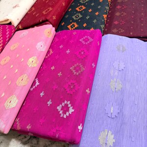 May include: A collection of colorful fabrics, each folded and displaying unique patterns. The fabrics range in color from light pink to deep burgundy, with gold and silver metallic accents. The patterns include geometric shapes and floral designs.