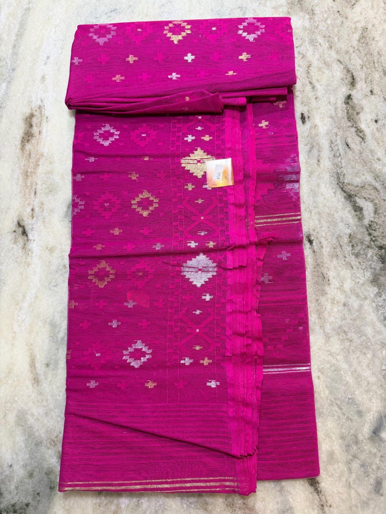 May include: A vibrant fuchsia textile with intricate geometric patterns in gold and silver. The fabric is folded, revealing the detailed design and texture. This textile is likely a traditional garment.