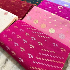 May include: A collection of folded fabric pieces in various colors, including fuchsia, pink, red, and navy. The fabrics feature intricate patterns with metallic accents, such as gold and silver, creating a textured and decorative appearance. The textiles are likely used for clothing or home decor.
