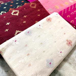 May include: A collection of folded fabric pieces in various colors, including white, burgundy, pink, and purple. Each piece features a floral or geometric pattern in contrasting colors. The fabrics appear to be lightweight and suitable for apparel or home decor.