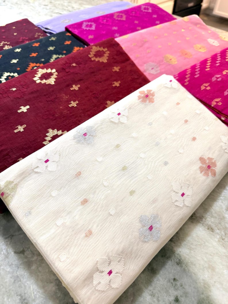 May include: A collection of folded fabric pieces in various colors, including white, burgundy, pink, and purple. Each piece features a floral or geometric pattern in contrasting colors. The fabrics appear to be lightweight and suitable for apparel or home decor.