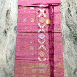 May include: Pink textile with gold and silver geometric patterns. The fabric has a central design of diamond shapes and a border with horizontal stripes. The textile is folded and appears to be new.