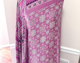 May include: A vibrant magenta fabric with an intricate floral and paisley pattern. The design includes white, black, and olive green accents. The fabric is draped over a black mannequin, showcasing the detailed print and texture.
