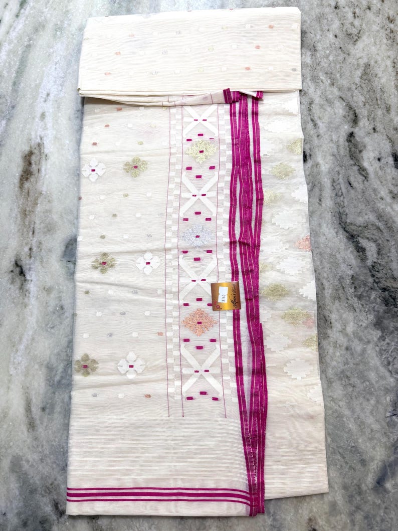 May include: A white fabric with a detailed pattern and a vibrant pink border and accents. The fabric features floral and geometric designs, with a folded section at the top. The overall aesthetic is elegant and detailed.