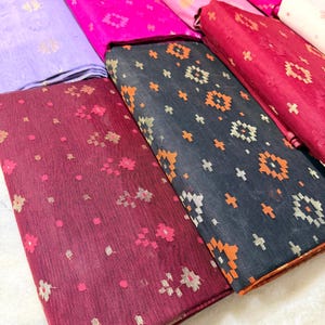 May include: A collection of folded fabric in various colors, including purple, pink, and burgundy. The fabrics feature floral and geometric patterns in contrasting colors. The textiles appear to be lightweight and suitable for clothing or home decor projects.