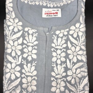 May include: A light gray tunic with white floral embroidery. The tunic features a round neckline and a center placket. The label reads "Lavish Lucknowi Chikan Kari" and indicates a size 40.
