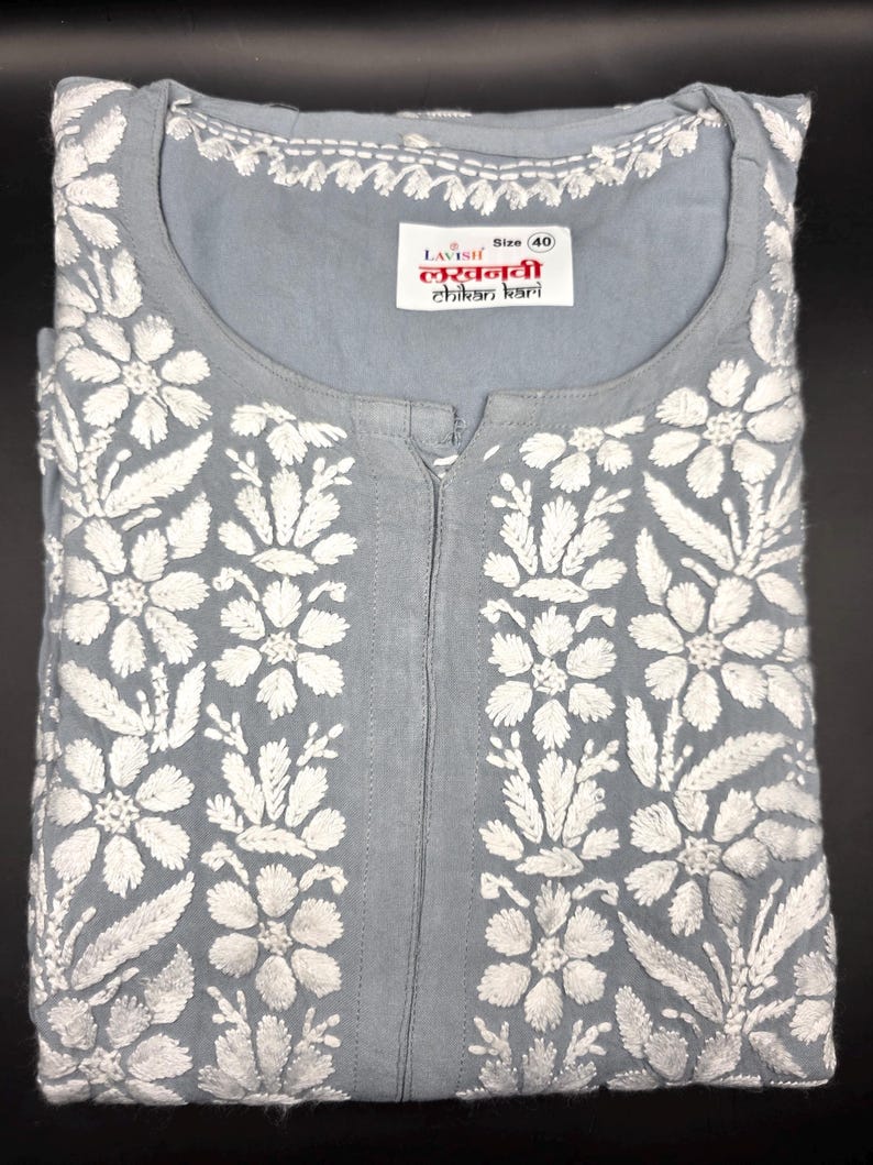 May include: A light gray tunic with white floral embroidery. The tunic features a round neckline and a center placket. The label reads "Lavish Lucknowi Chikan Kari" and indicates a size 40.