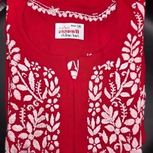 May include: A red tunic with white floral embroidery. The tunic has a round neckline with white trim and a small slit at the chest. The label reads "LAVISH" and "Size 38".