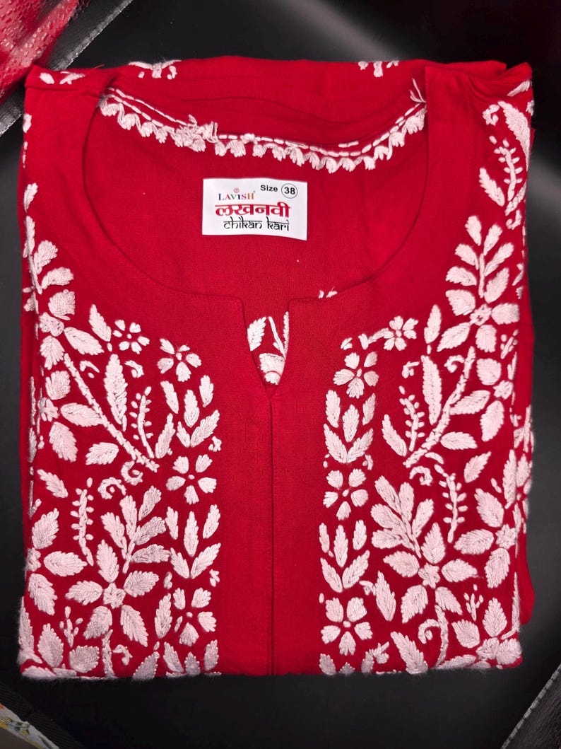 May include: A red tunic with white floral embroidery. The tunic has a round neckline with white trim and a small slit at the chest. The label reads "LAVISH" and "Size 38".