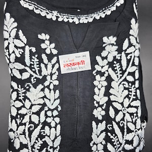 May include: Black tunic with white floral embroidery. The tunic features a V-neck and a white embroidered neckline. A label with text is visible on the front. Size 44.