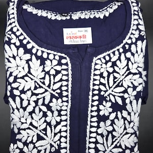 May include: Navy blue tunic with intricate white floral embroidery. The tunic features a round neckline and a split front. A label with text is visible near the neckline. Size 46.