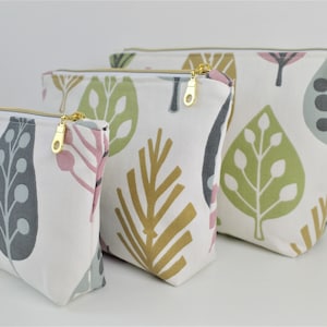 Peut inclure: Trois pochettes zippées avec un fond blanc et un motif de feuilles colorées. Les pochettes sont de tailles différentes et sont alignées de la plus grande à la plus petite.