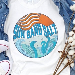 May include: White t-shirt with a round graphic design featuring a sun, waves, and the text "Sun Sand Salt".