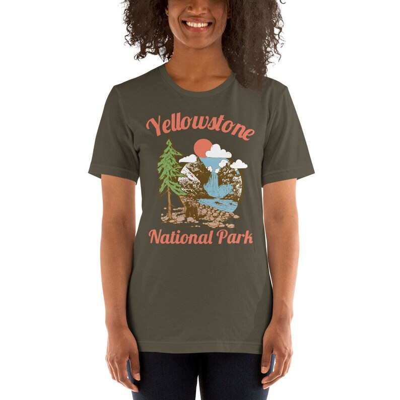 May include: A dark green t-shirt with a vintage-style illustration of a mountain scene with a waterfall, a tree, and a sun. The text "Yellowstone National Park" is printed in orange on the shirt.