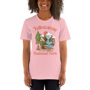 May include: Pink t-shirt with a vintage-style graphic of a mountain scene with a waterfall and the text "Yellowstone National Park".