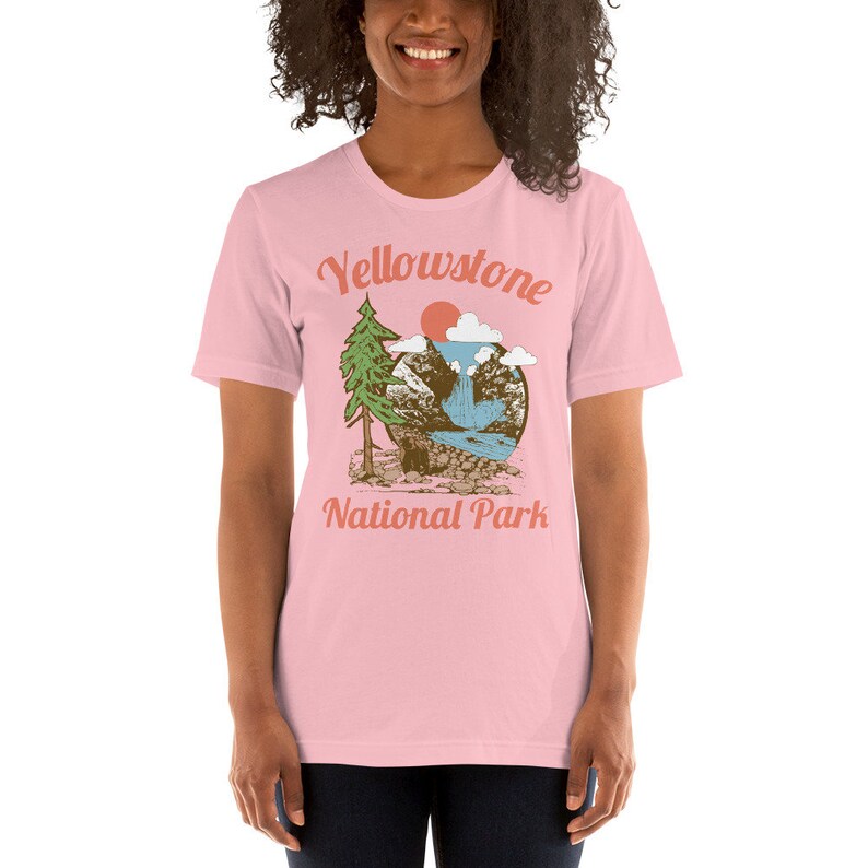 May include: Pink t-shirt with a vintage-style graphic of a mountain scene with a waterfall and the text "Yellowstone National Park".