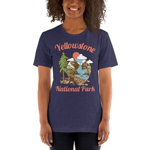May include: A navy blue t-shirt with a vintage-style graphic of a mountain scene with a waterfall, a pine tree, and a red sun. The text "Yellowstone National Park" is printed in a peachy-orange color.