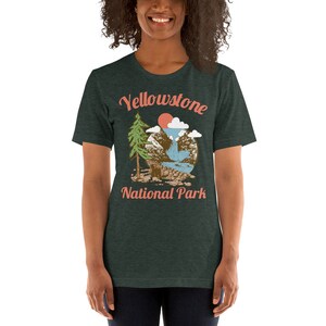 May include: A dark green t-shirt with a vintage-style illustration of a mountain scene with a waterfall, a pine tree, and a red sun. The text "Yellowstone National Park" is printed in a light pink font.