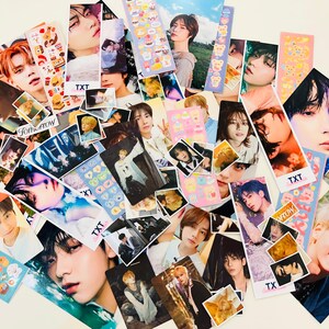 May include: A collection of colorful photo cards featuring various K-pop idols. The cards feature images of the idols in different poses and outfits, with some cards also including text such as "TXT" and "Tomorrow X Together".