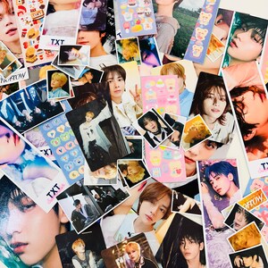 May include: A collection of colorful photo cards featuring various K-pop idols. The cards are decorated with stickers and text, including the words "TXT" and "Tomorrow X Together".