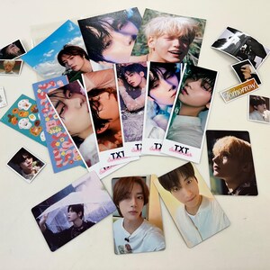 May include: A collection of photo cards featuring a K-pop boy band. The cards are printed with various images of the band members, including close-ups of their faces and full-body shots. The cards are decorated with the band's name, "TXT", and the word "Tomorrow".