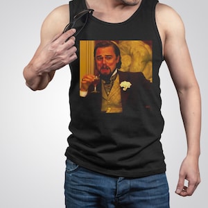 Può includere: Una canotta nera con un'immagine stampata di Leonardo DiCaprio che tiene un bicchiere di vino e guarda lo spettatore. L'immagine è tratta dal film Il lupo di Wall Street.