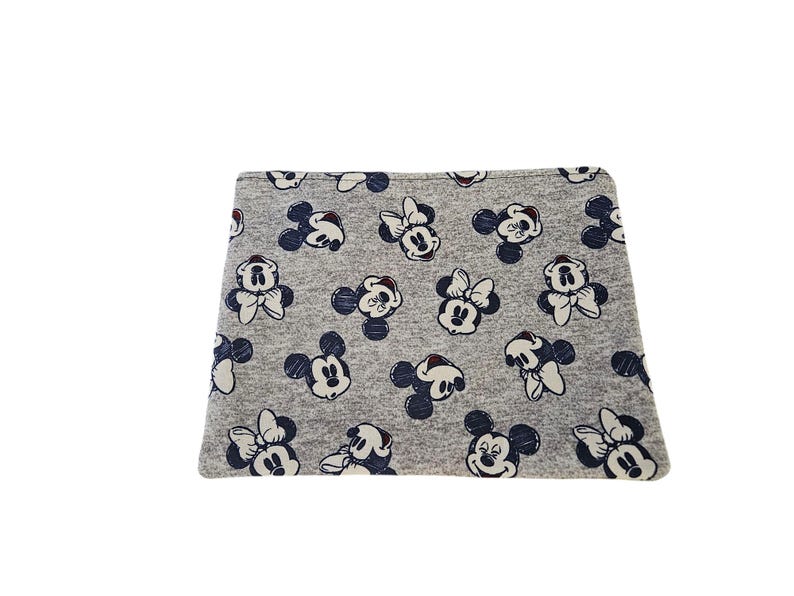 May include: A grey fabric with a repeating pattern of Mickey and Minnie Mouse. The cartoon characters are in white and navy blue, creating a playful design. The fabric appears soft and suitable for various applications, such as clothing or accessories.