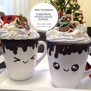 May include: Two white ceramic mugs with chocolate sauce drizzled down the sides. Each mug has a cute cartoon face and is topped with whipped cream, marshmallows, and a gingerbread man cookie. The mugs are on a white surface with a Christmas tree in the background. The text "PDF TUTORIAL CHRISTMAS CHOCO MUGS KAWAII INCLUDE FACE SVG-PNG FILES" is on a white circle in the upper right corner of the image.