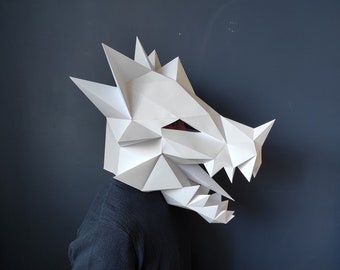 May include: A white paper dragon mask with a geometric design. The mask is worn by a person with a dark blue sweater.