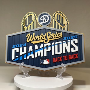 以下が含まれることがあります： 「World Series Champions 2024-2025 Back to Back」の文字が入った、紺色と金色の野球チャンピオンシップサイン。MLBのロゴとチームロゴが特徴です。