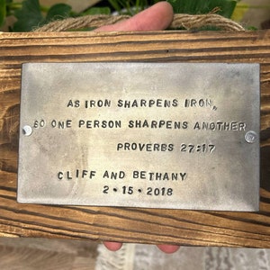 May include: A wooden plaque with a metal plate inset. The metal plate has the text "As iron sharpens iron, so one person sharpens another. Proverbs 27:17. Cliff and Bethany 2.15.2018" engraved on it.