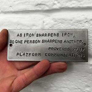 May include: A silver metal plaque with the text "AS IRON SHARPENS IRON, SO ONE PERSON SHARPENS ANOTHER, PROVERBS 27:17 PLATFORM COMMUNICATIONS".