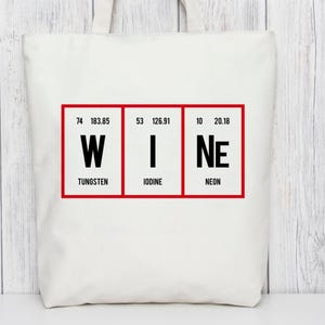 Op de afbeelding: Een witte draagtas met het woord "WINE" gespeld met behulp van de elementen van het periodiek systeem: Wolfram, Jodium en Neon. De elementen worden weergegeven in rode vakken met hun atoomnummers en gewichten.