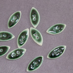 Könnte beinhalten: Zehn grüne und weiße Keramikknöpfe mit jeweils zwei Löchern. Die Knöpfe sind länglich oval geformt.