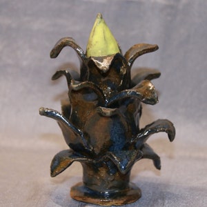 Könnte beinhalten: Eine Keramikskulptur eines stilisierten Ananasses mit grüner Spitze und dunkelblauer Glasur. Die Skulptur hat eine strukturierte Oberfläche und ist im rustikalen Stil gefertigt.