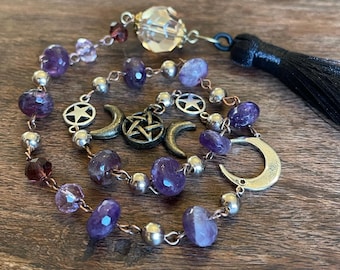 May include: A purple amethyst crystal beaded necklace with silver and copper chain links. The necklace features a clear crystal pendant, silver crescent moon charms, a pentagram charm, and a black tassel.