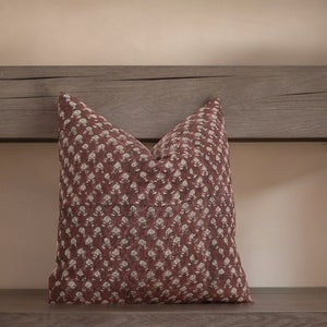 May include: A burgundy throw pillow with a white floral pattern. The pillow is sitting on a wooden surface.