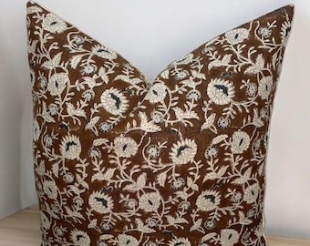 May include: A brown throw pillow with a white floral pattern. The pillow is made of a soft, textured fabric and has a subtle sheen.