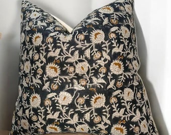 May include: A decorative throw pillow with a dark navy blue background and a floral pattern in cream and brown. The pillow is resting on a light wood surface, adding a touch of elegance to any room's decor.