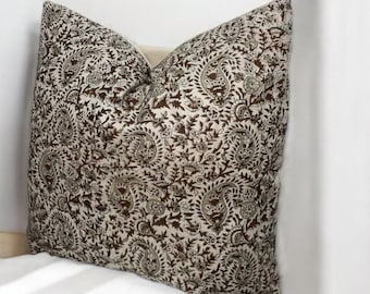 May include: A brown and cream patterned throw pillow with a paisley design. The pillow is sitting on a white surface.