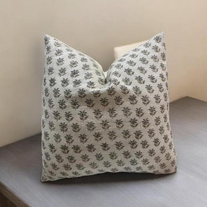 May include: A white cushion with a green floral pattern. The cushion is made of a soft, linen fabric and has a subtle sheen.